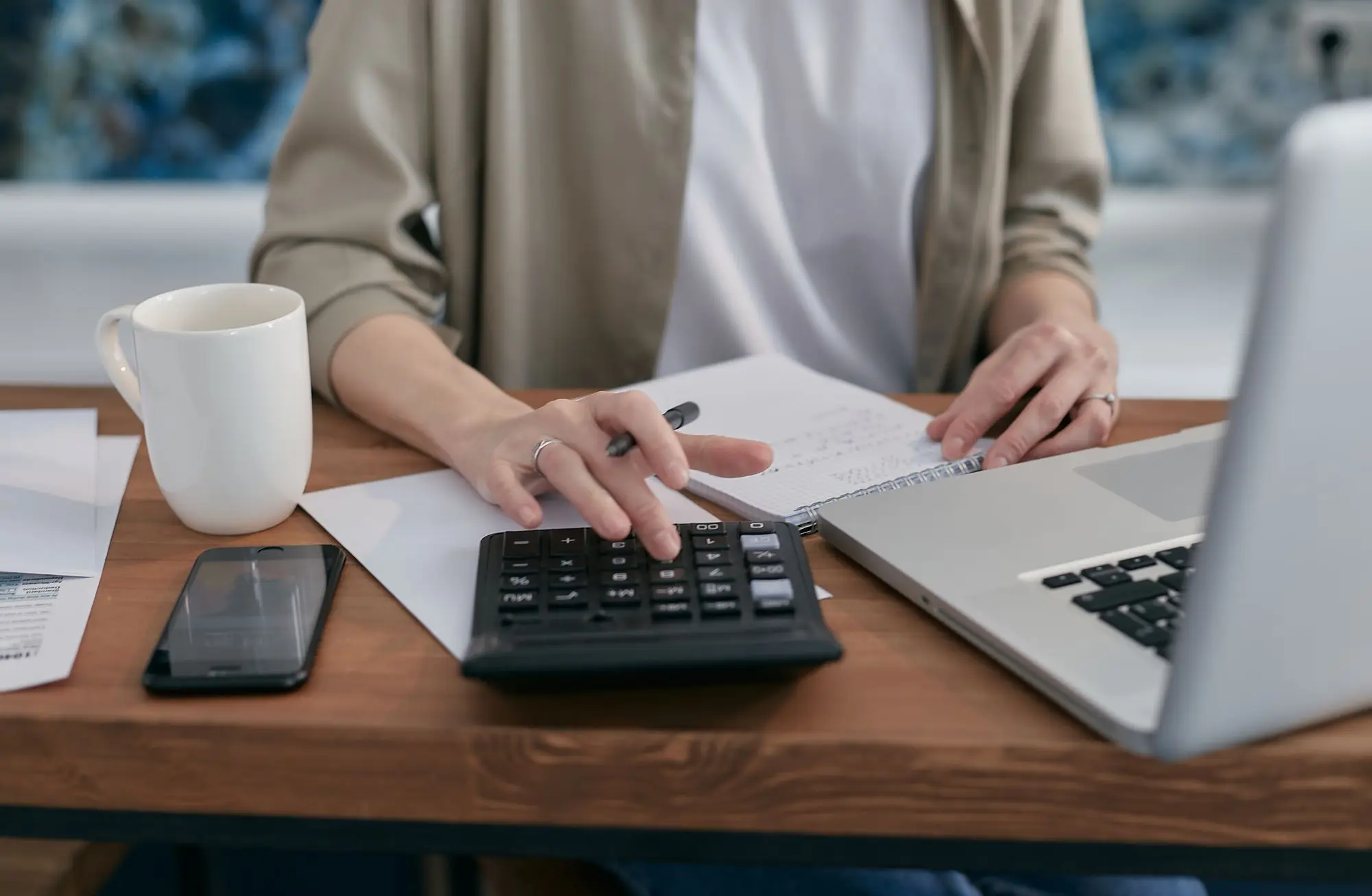 Business owner tallying debts and assets on a calculator beside a notebook and laptop