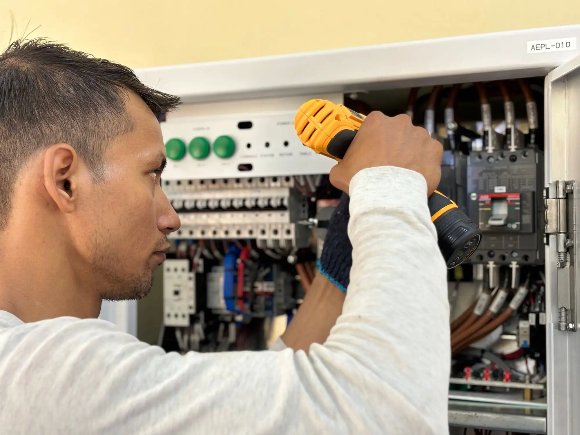 Electrician working alone on an open switchboard with a cordless drill, now running the business as sole owner