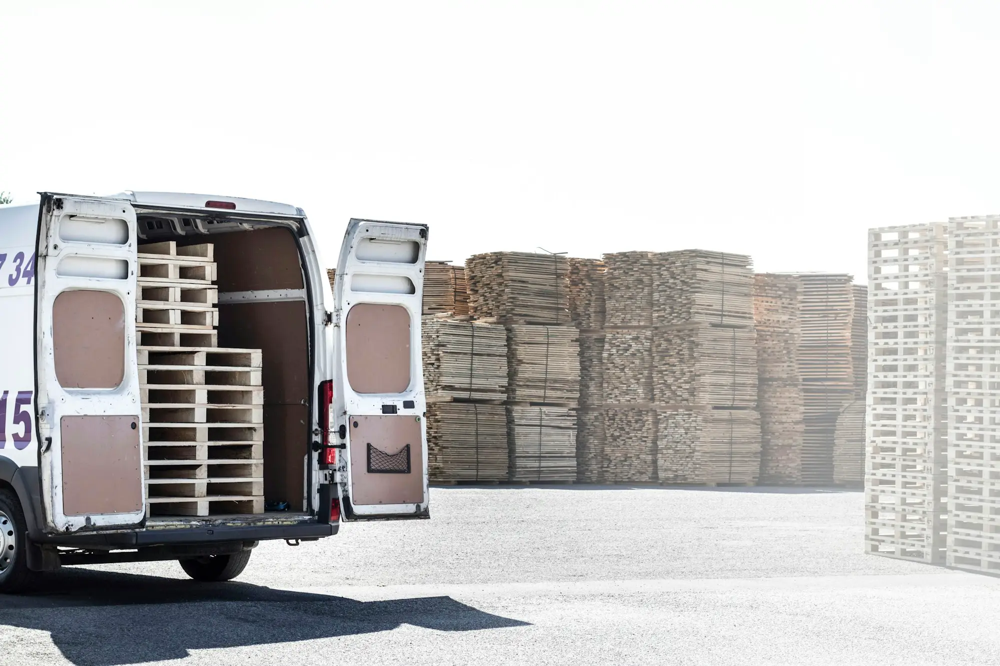 Courier van with doors open being loaded beside stacked pallets